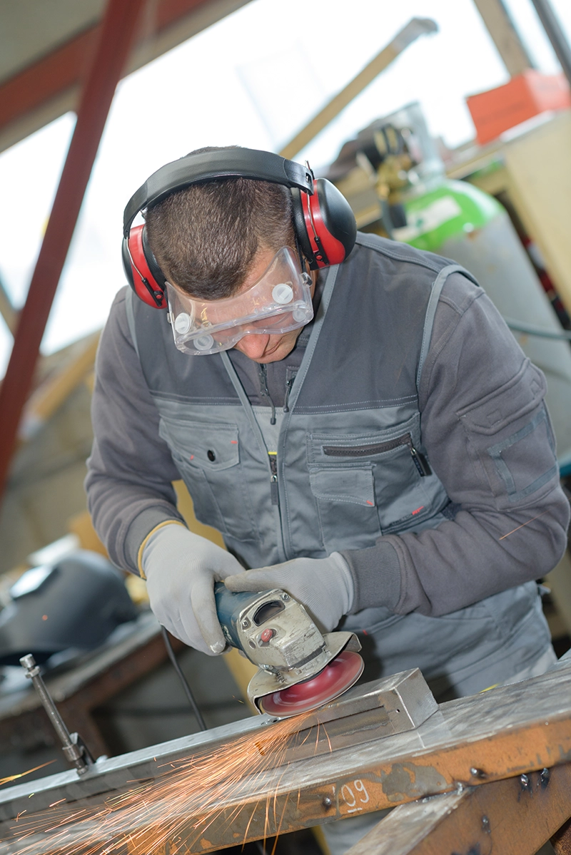 Worker using a grinder tool while wearing eye and hearing protection