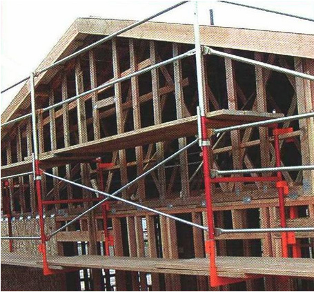 The installed Jax Scaffold System composed of galvanized metal guardrails, scaffold planks, and metal support brackets, which are supported by the vertical studs of the walls.