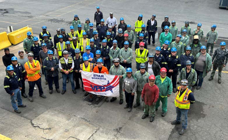 A large group of McWane Ductile workers stand in a semi-circle formation, while 4 workers in the front row display their VPP Star flag in Phillipsburg, NJ.