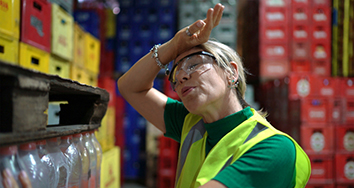 Woman in a heated warehouse, wiping her brow.