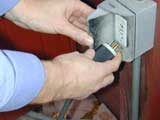 worker plugging an electrical cord into an electrical outlet with their fingers on the prongs of the plug