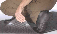 person kneeling on a non-slip mat, wearing non-slip shoes, lifting the corner of the mat to show the grip surface on the underside