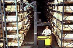 Figure 2. Triplex mast in narrow aisle rider reach truck. Note that the forklift is removing stock from a rack. Foot and truck traffic in the opposite aisle way should be controlled to prevent injury from falling materials.