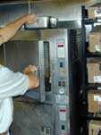 Image of a worker reaching above an oven while removing food.