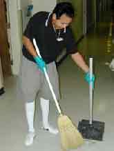 young worker sweeping broken glass into a long-handled dustpan.