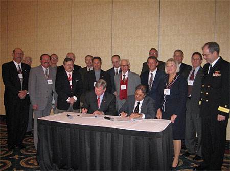 Seated from left to right at the signing table are: Malcolm P. Branch, President, Virginia Ship Repair Association and Leo Edwards, Acting Area Director, OSHA Norfolk Area Office. Standing to the right of the signing table: U. S. Congresswoman, Thelma Drake and RDML John Clarke Orzalli. Standing behind the signatories are several of the Partnership participants.