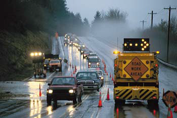 Vehicles being guided down a wet road through construction cones