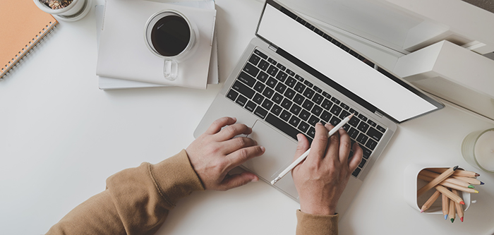 Top-down shot of person at a desk with coffee and pencils, typing on a laptop