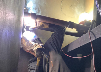 Worker welding pipes in tightly confined space