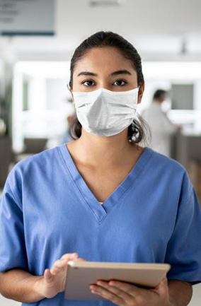 Nurse wearing mask and scrubs, working on tablet