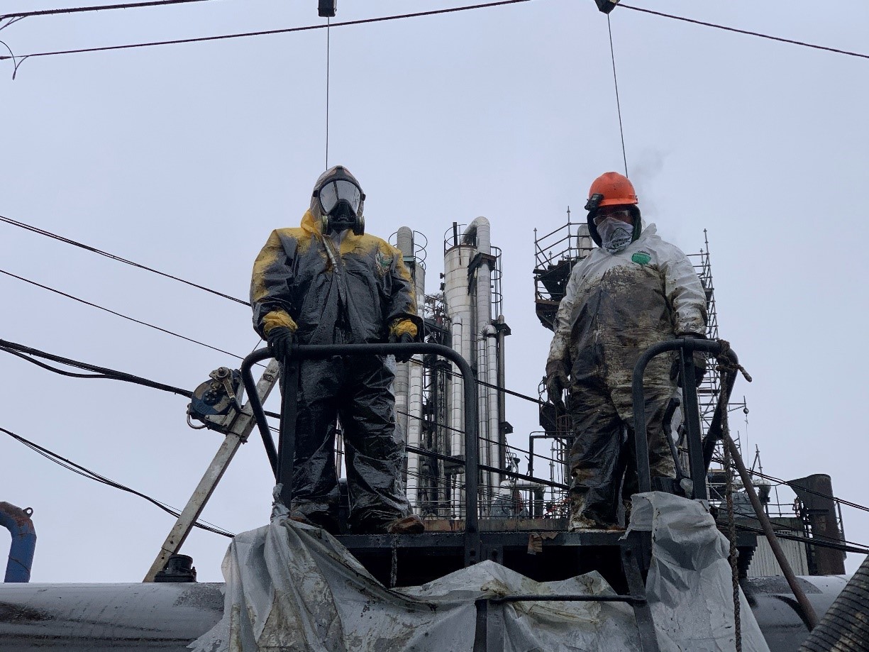 K-Plus employees, respectively assuming the duties of permit-required confined space entrant and attendant, cleaning a rail car.